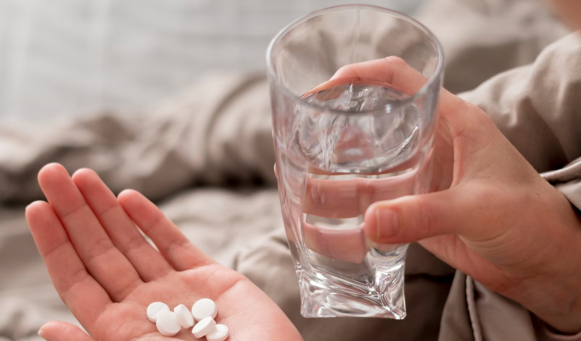 Человек держит стакан воды и таблетки, готовясь к приему варфарина для предотвращения тромбообразования.