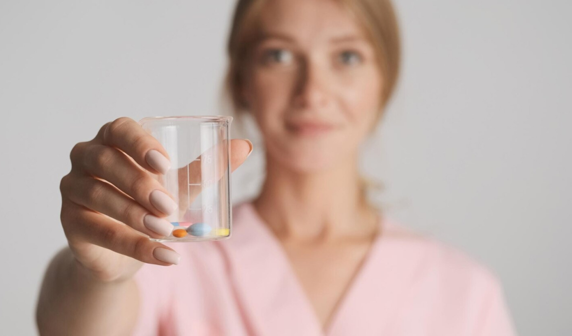 Женщина в розовом халате с стаканом таблеток принимает варфарин для профилактики тромбообразования